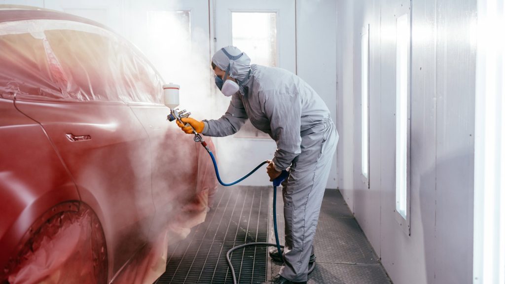 Operator in a paint booth spraying a car body, demonstrating ATEX Fans in paint and varnish extraction systems.