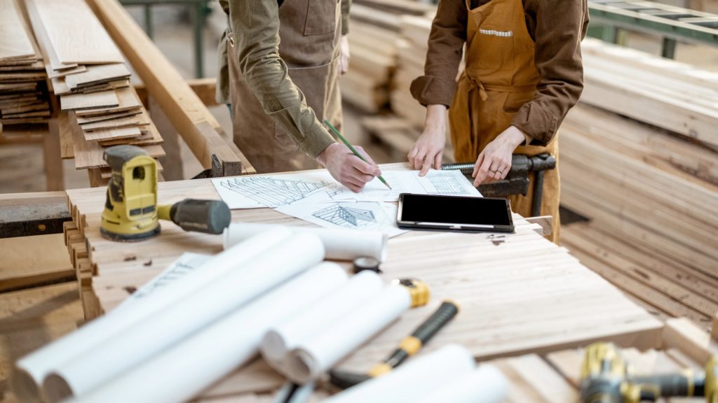 Carpenters reviewing woodwork plans in a workshop, highlighting ATEX Fans for dust- and fume-controlled carpentry environments.
