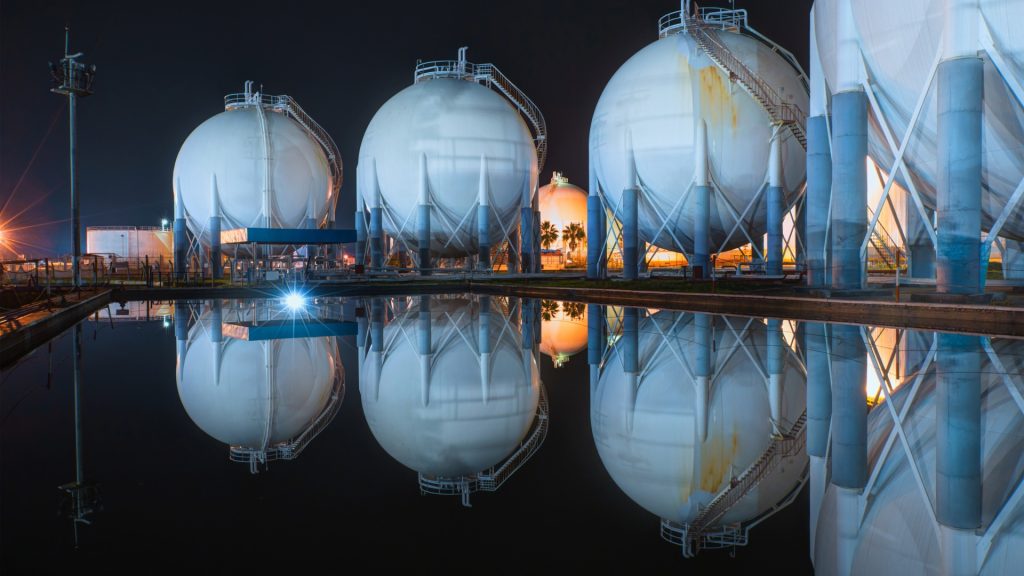 Spherical fuel storage tanks reflected in water at night, illustrating ATEX Fans safeguarding liquid and gaseous fuel warehouses.