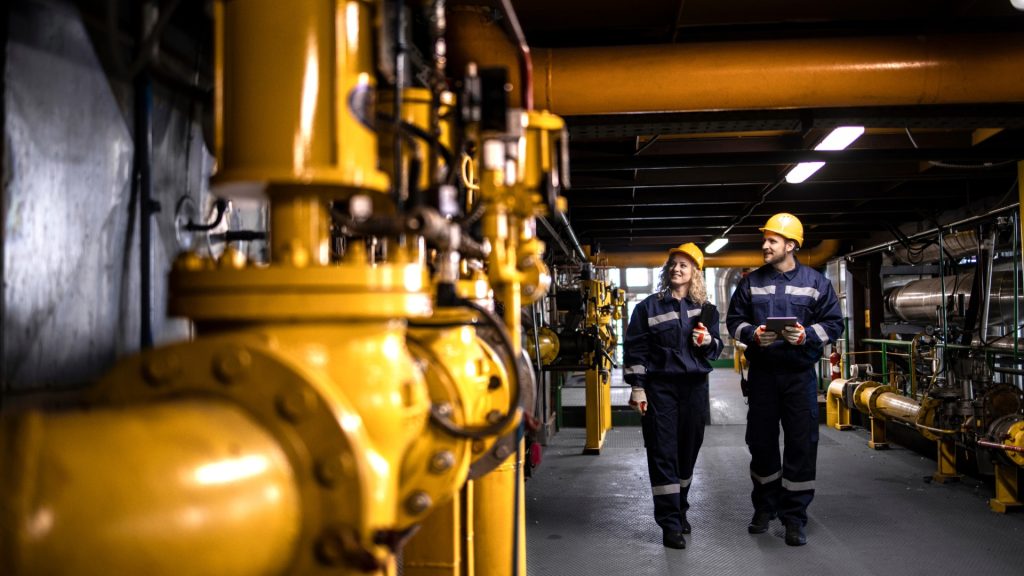 Process engineers inspecting yellow pipework in a plant served by heavy duty fans for fume extraction.